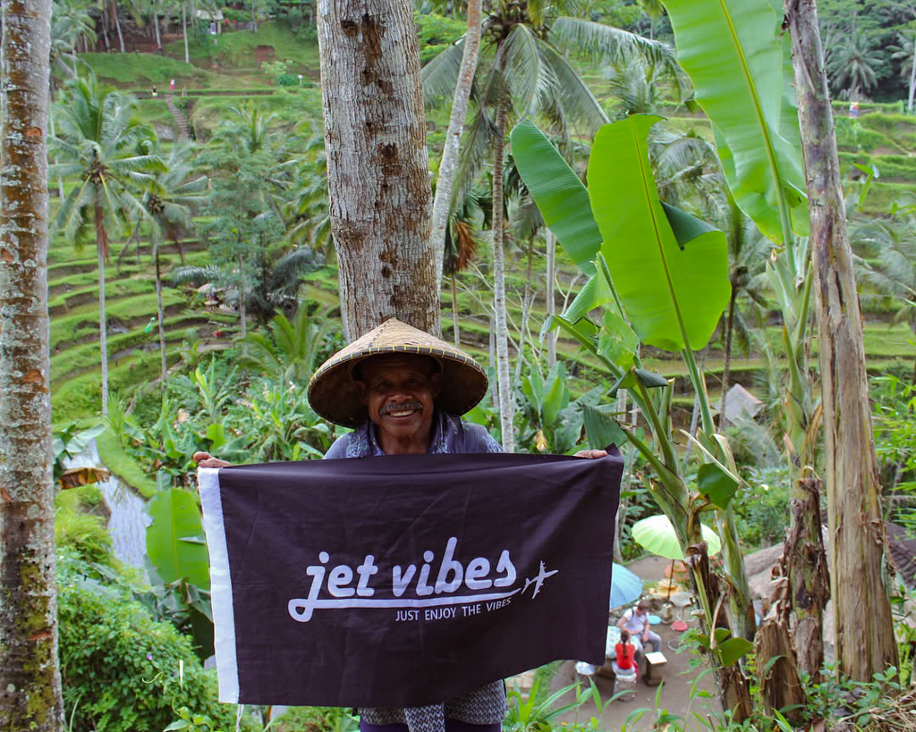 Bali local holding the Jet Vibes flag in a tropical travel setting